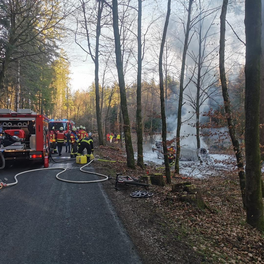 Feuerwehreinsatz mit umgekipptem Auto und Rauch im Wald, Feuerwehrleute und Ersthelfer vor Ort
