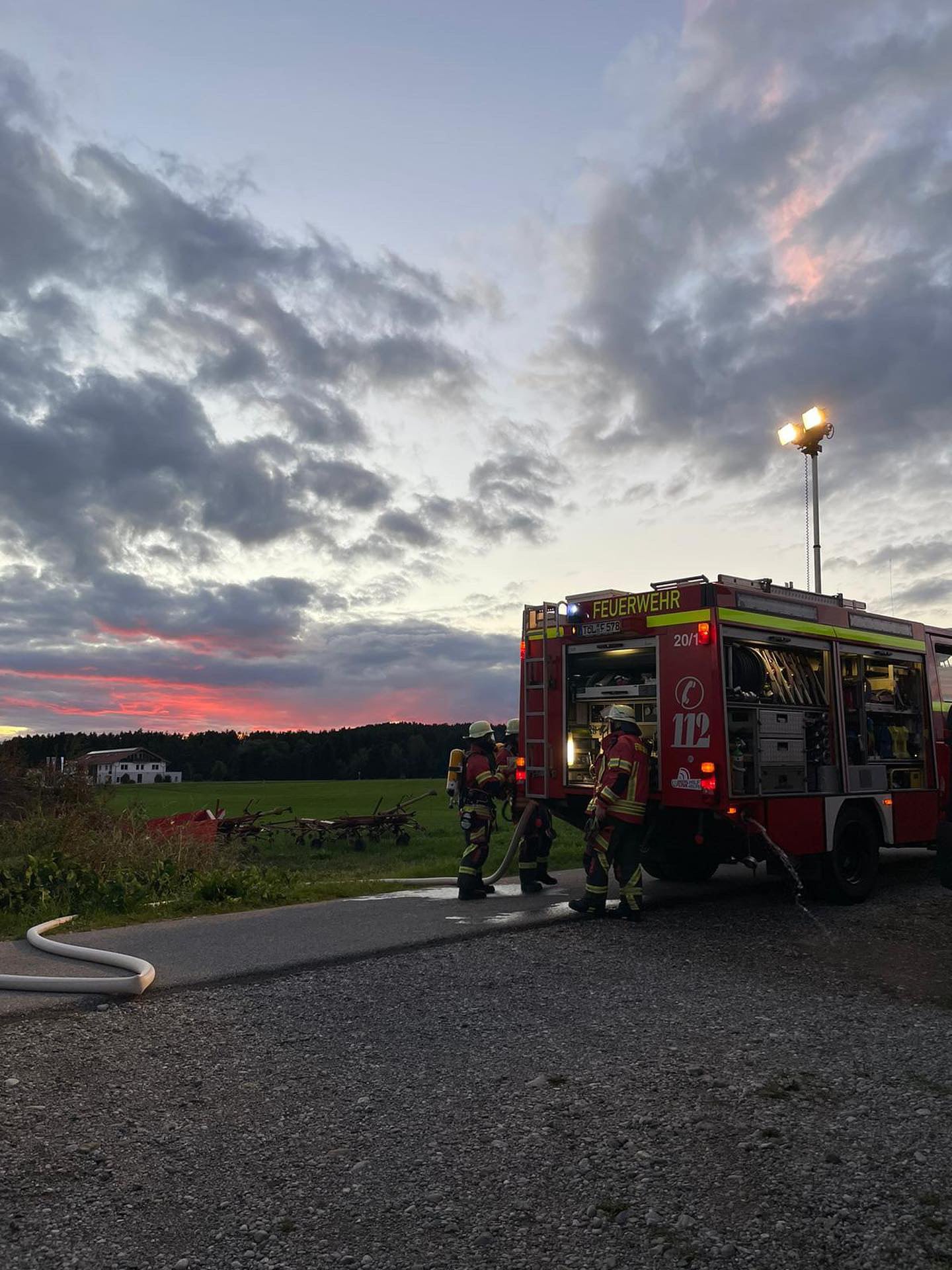Feuerwehrfahrzeug mit drei Feuerwehrleuten bei Sonnenuntergang, Ebenen und Wald im Hintergrund mit Wolken