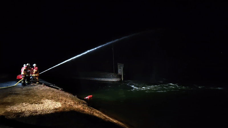Feuerwehrübung bei Nacht, Wasser schießt aus Feuerwehrschlauch in einen See